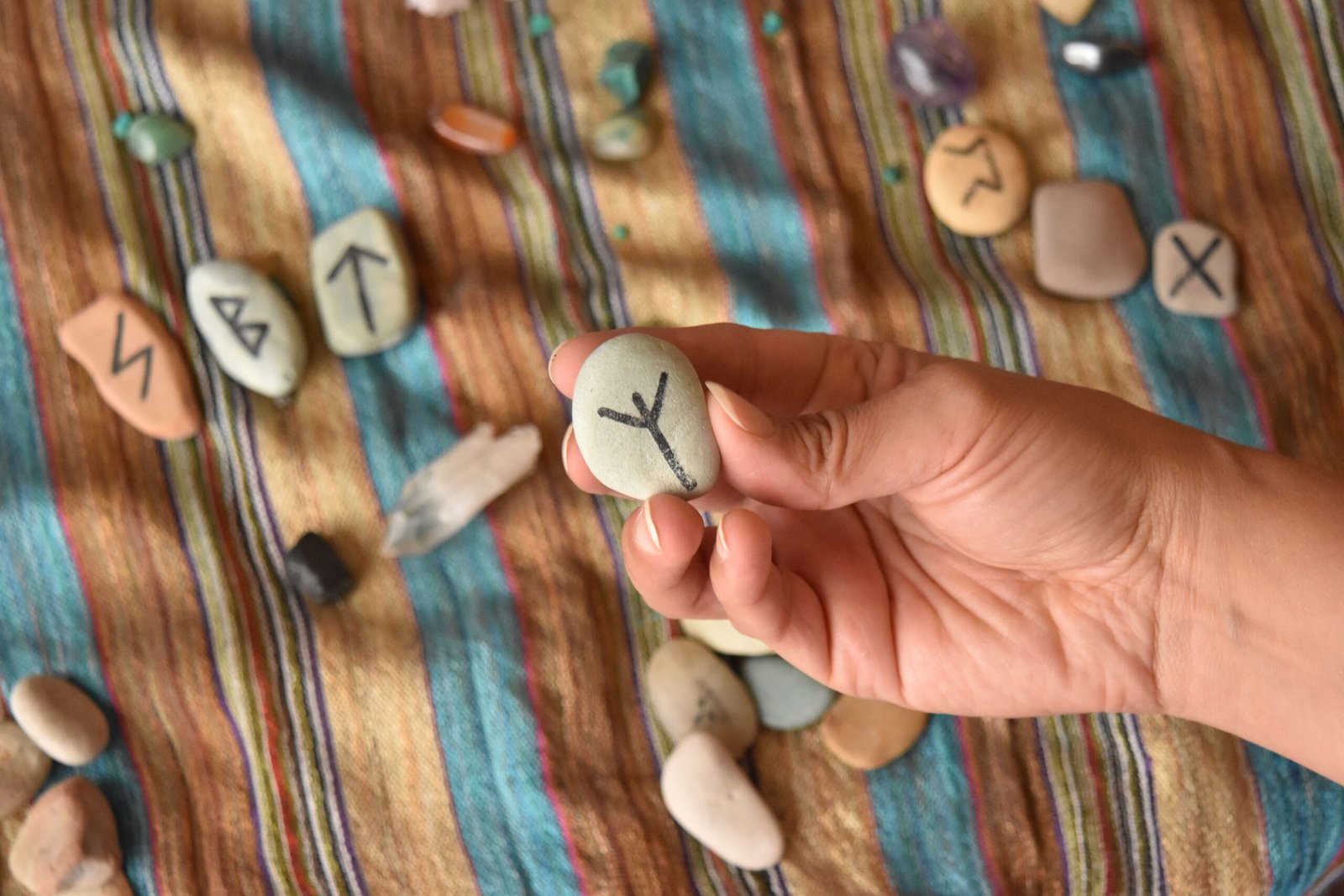 A hand holds a rune stone with runes scattered on colorful striped fabric.
