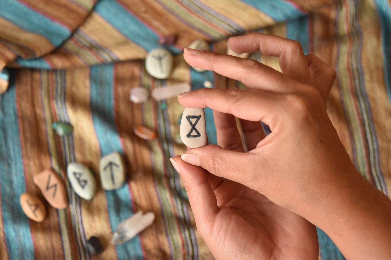 Close-up of hands holding a rune stone with various stones on a colorful fabric background.