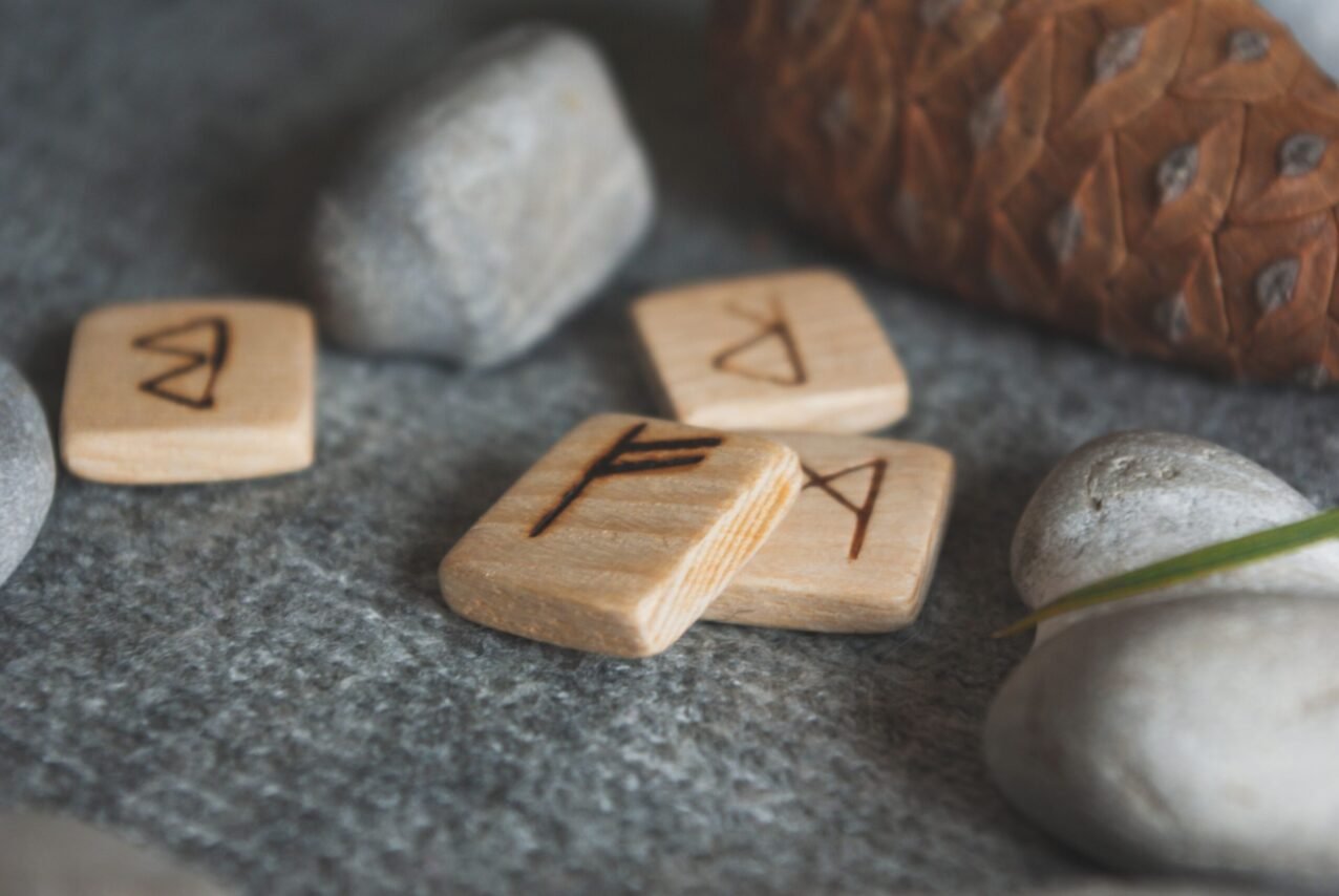 From above set of wooden runes and stones placed in knitted wool blanket near fir cone
